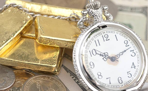 Voici un texte alternatif approprié pour l’image que tu as envoyée : Texte alternatif : Une montre de poche argentée à chiffres romains repose sur une pile de lingots d'or brillants, entourée de pièces de monnaie argentées et de billets de banque américains, illustrant la richesse et la valeur du temps.